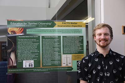 Student standing by his group’s augmented reality poster