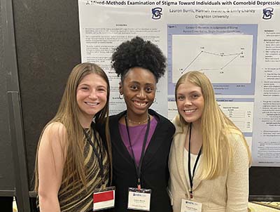 Lauren Burris displays research poster with student colleagues.