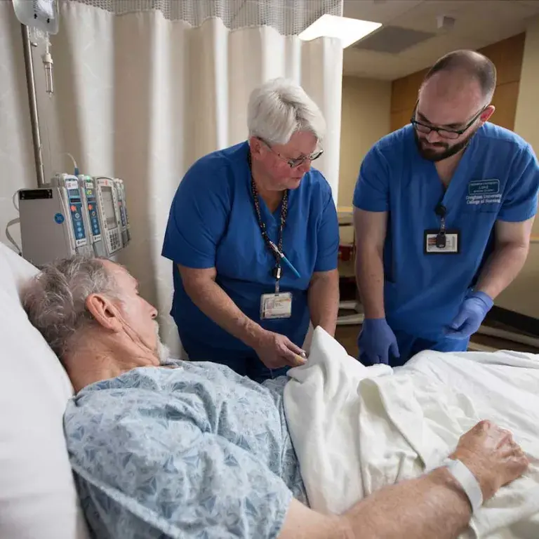 Two nurses assisting a patient in a hospital bed