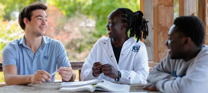 Three students smiling in white coats around a table