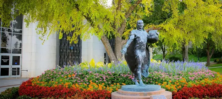 Jesuit statue amidst colorful flowers.
