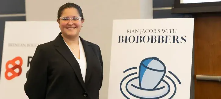 Rian Jacobs stands proudly beside company logo at event.