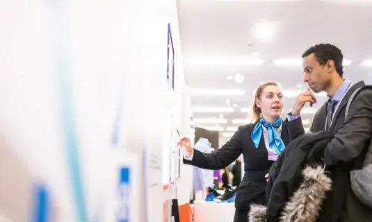 Two people in business attire talking in front of a whiteboard