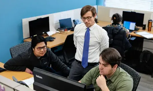 Three people strategizing around a computer.
