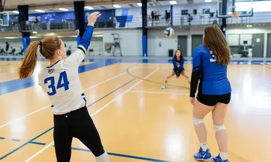 Female students playing volleyball on indoor court.
