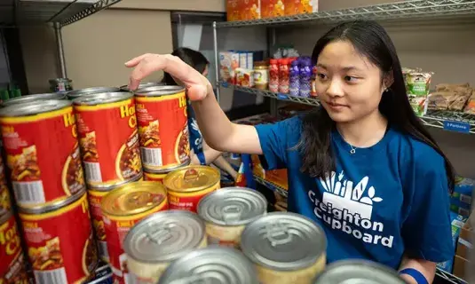 Student grabbing a canister of chips from shelf.