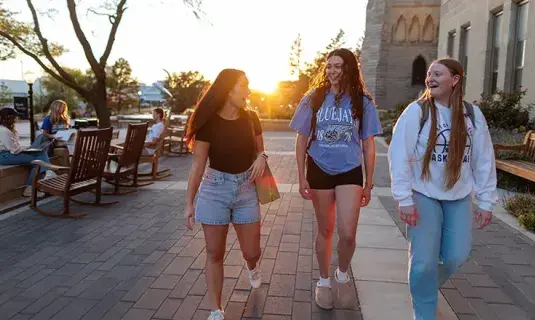 Three students walking on campus at sunset.