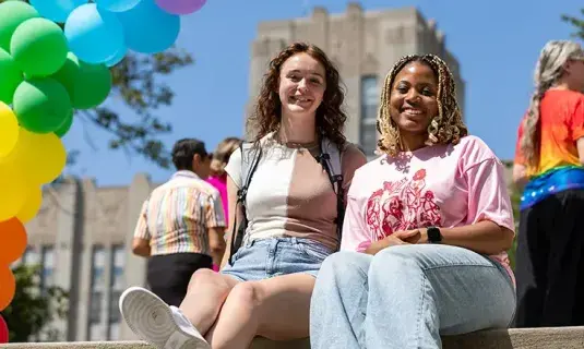 Students sitting together on campus with multi-colored balloons in the background.