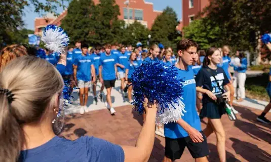 Students walking in mass down campus mall on sunny day.
