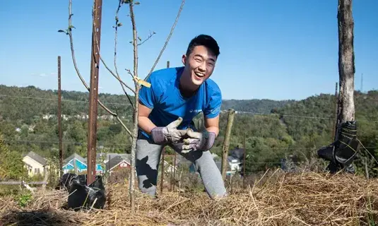 Student smiling while planting a tree.