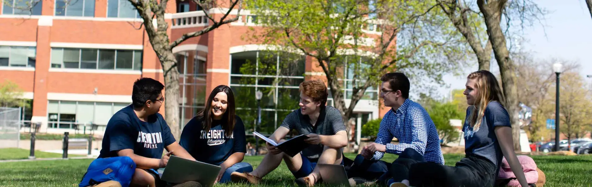 Heider students studying outside in shade on grassy knoll.