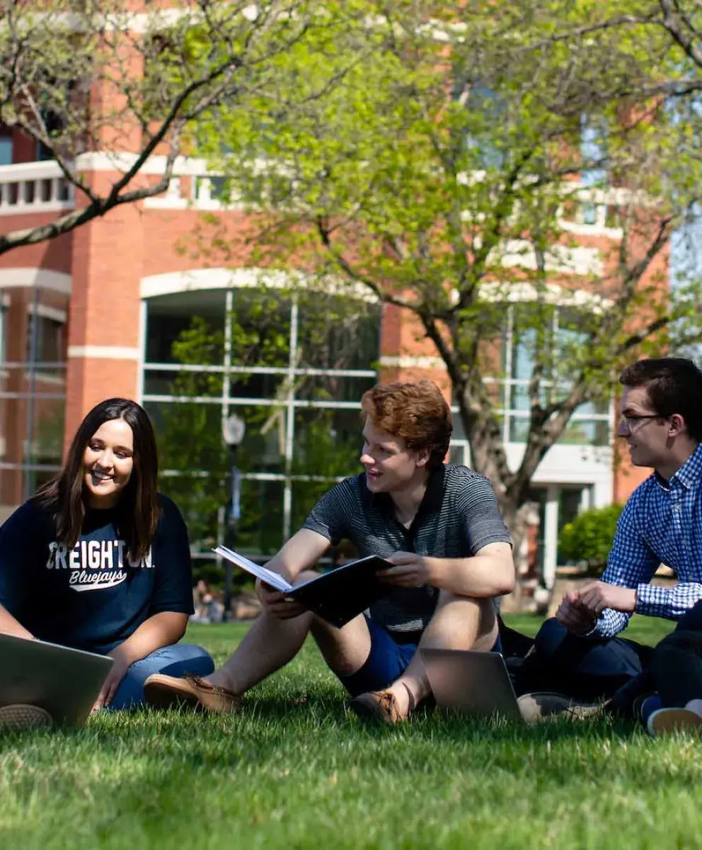 Heider students studying outside in shade on grassy knoll.