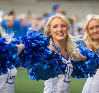 Bluejay cheerleaders cheering for crowd and waving blue pom poms.