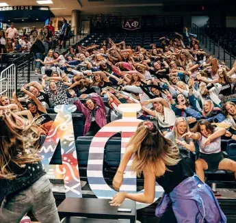 Students bending their bodies to the side in unison while seated in auditorium audience.