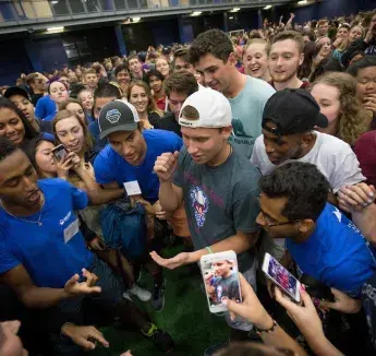 Welcome week activity with crowd of people in huddle with phones out taking photos.