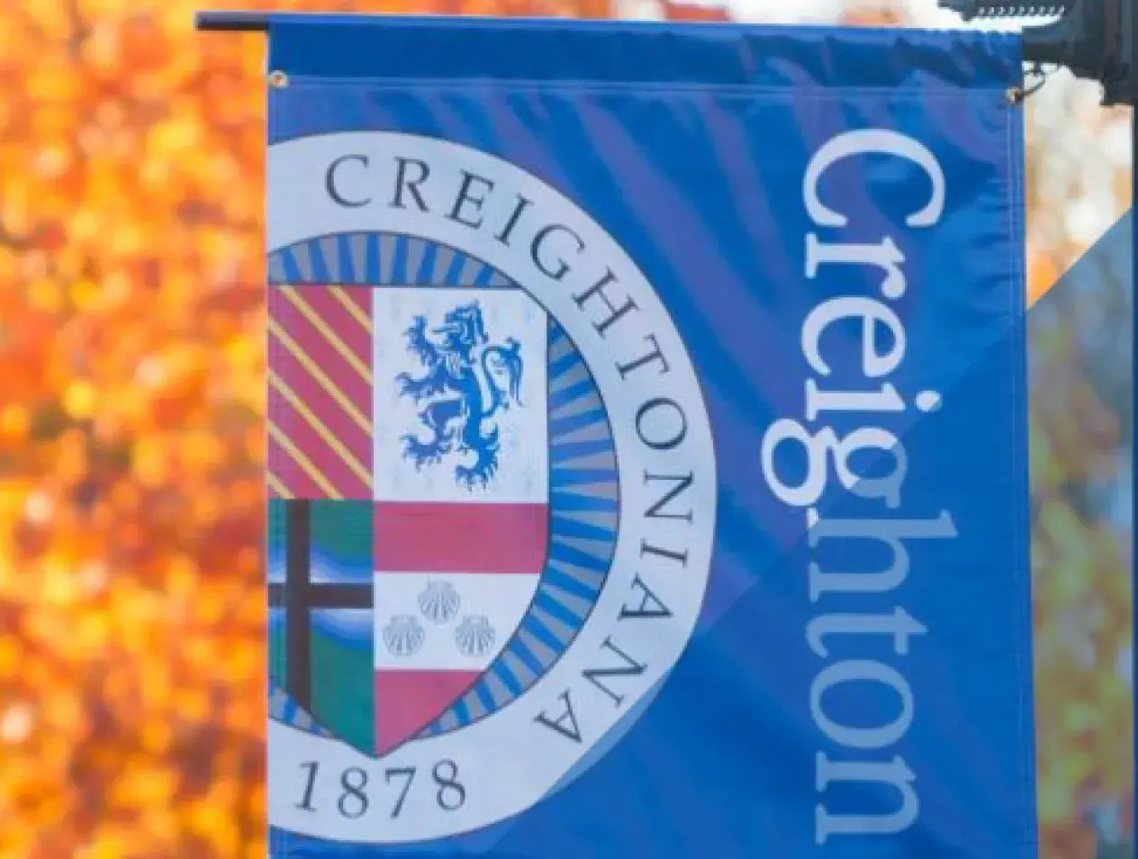 Creighton banner on campus with orange shining leaves on tree branches
