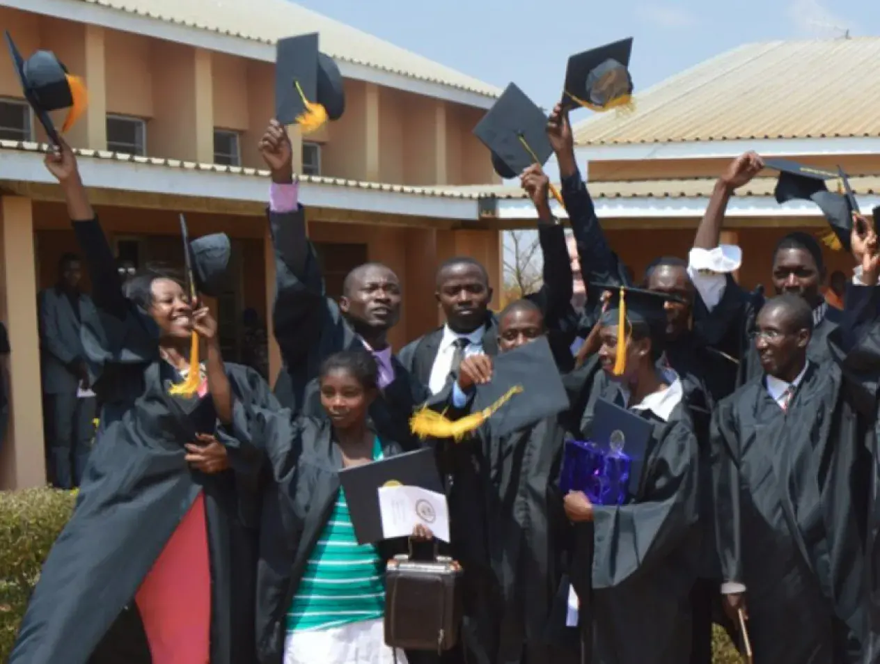 A group of Jesuit Worldwide Learning graduates holding their caps in the air