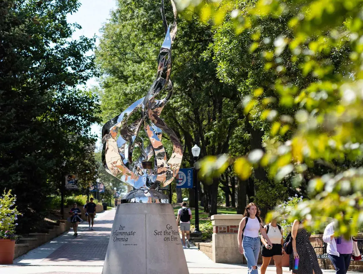 Students walking outdoors on Creighton campus by flame statue