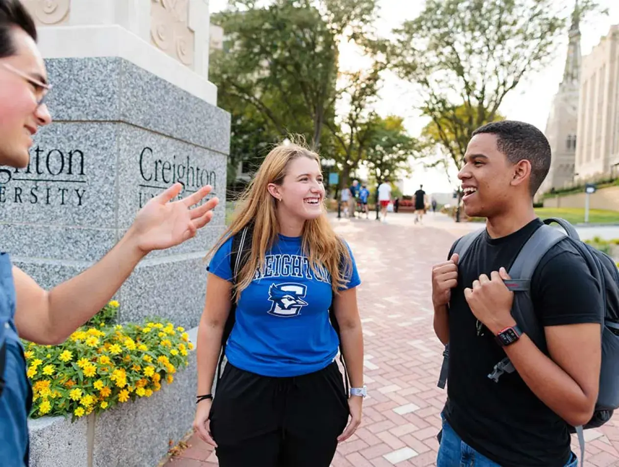 Three students gathered by the Creighton pillar outdoors