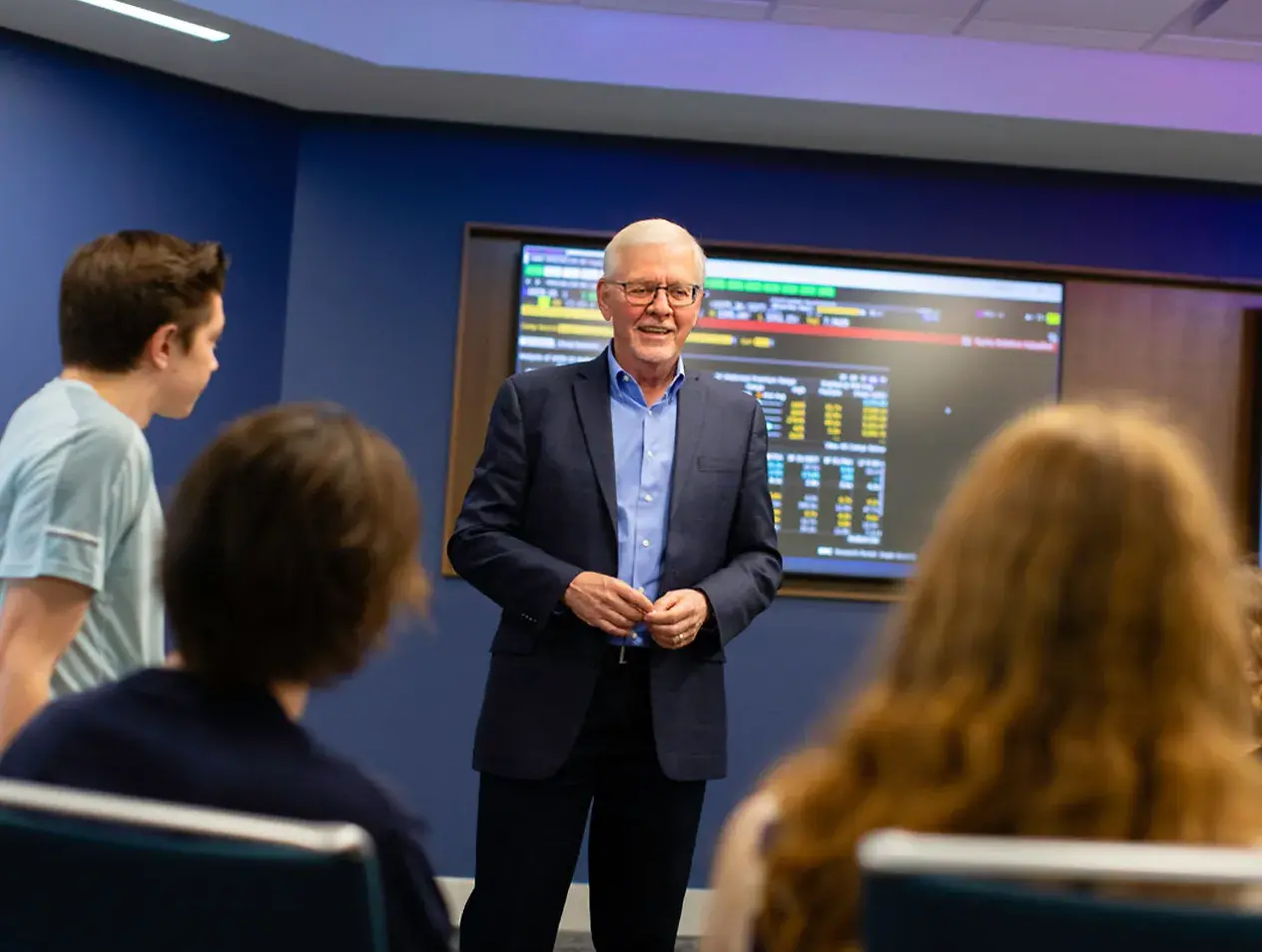 Instructor with students in the Portfolio Practicum classroom showing data on video monitors.