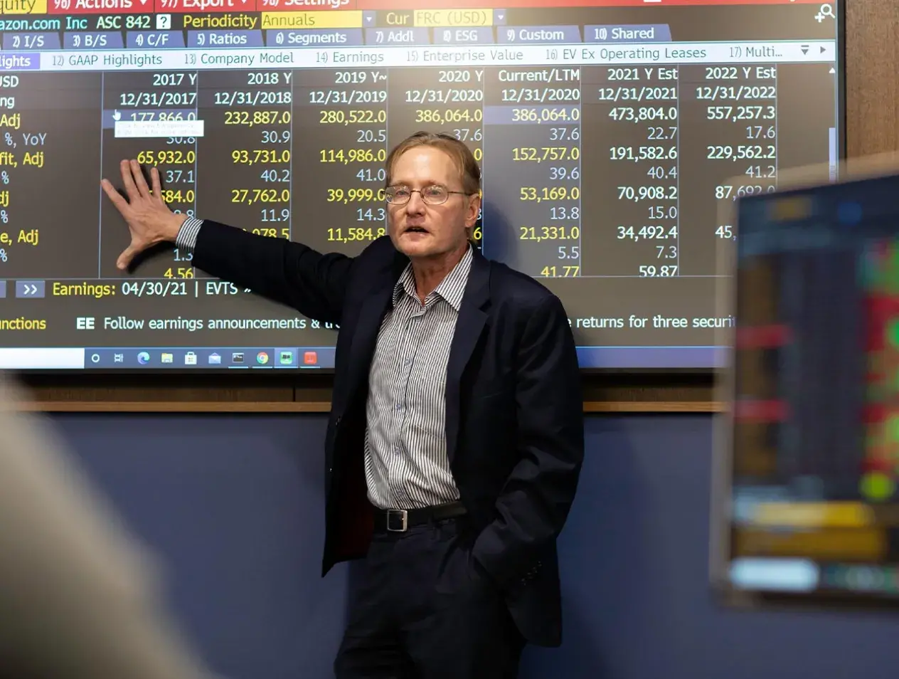 Instructor in front smart board displaying stocks