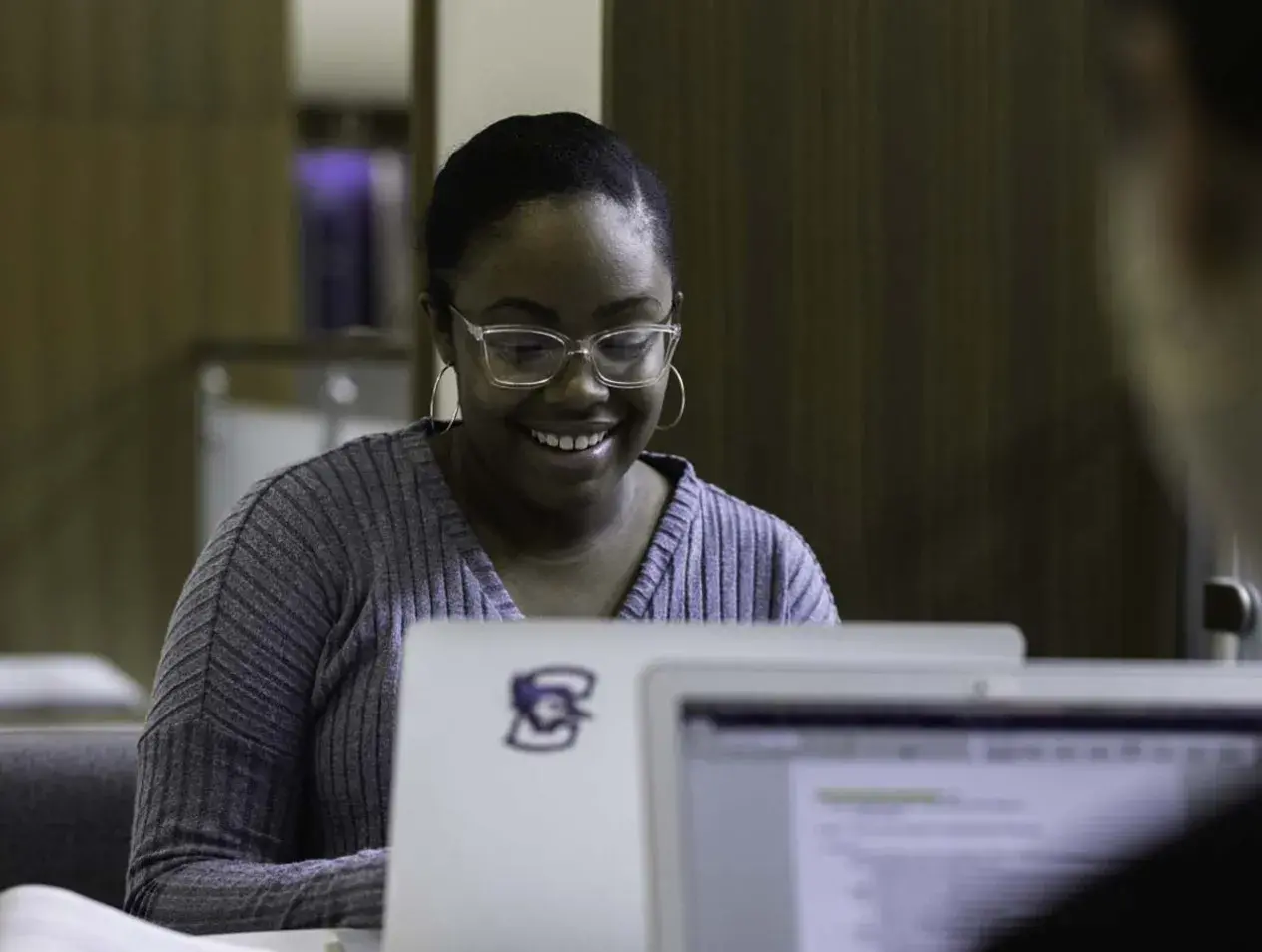 Female student smiling while working on laptop with Bluejay logo sticker.
