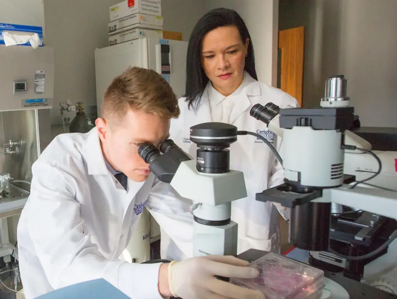 Man looking through microscope with woman observing.