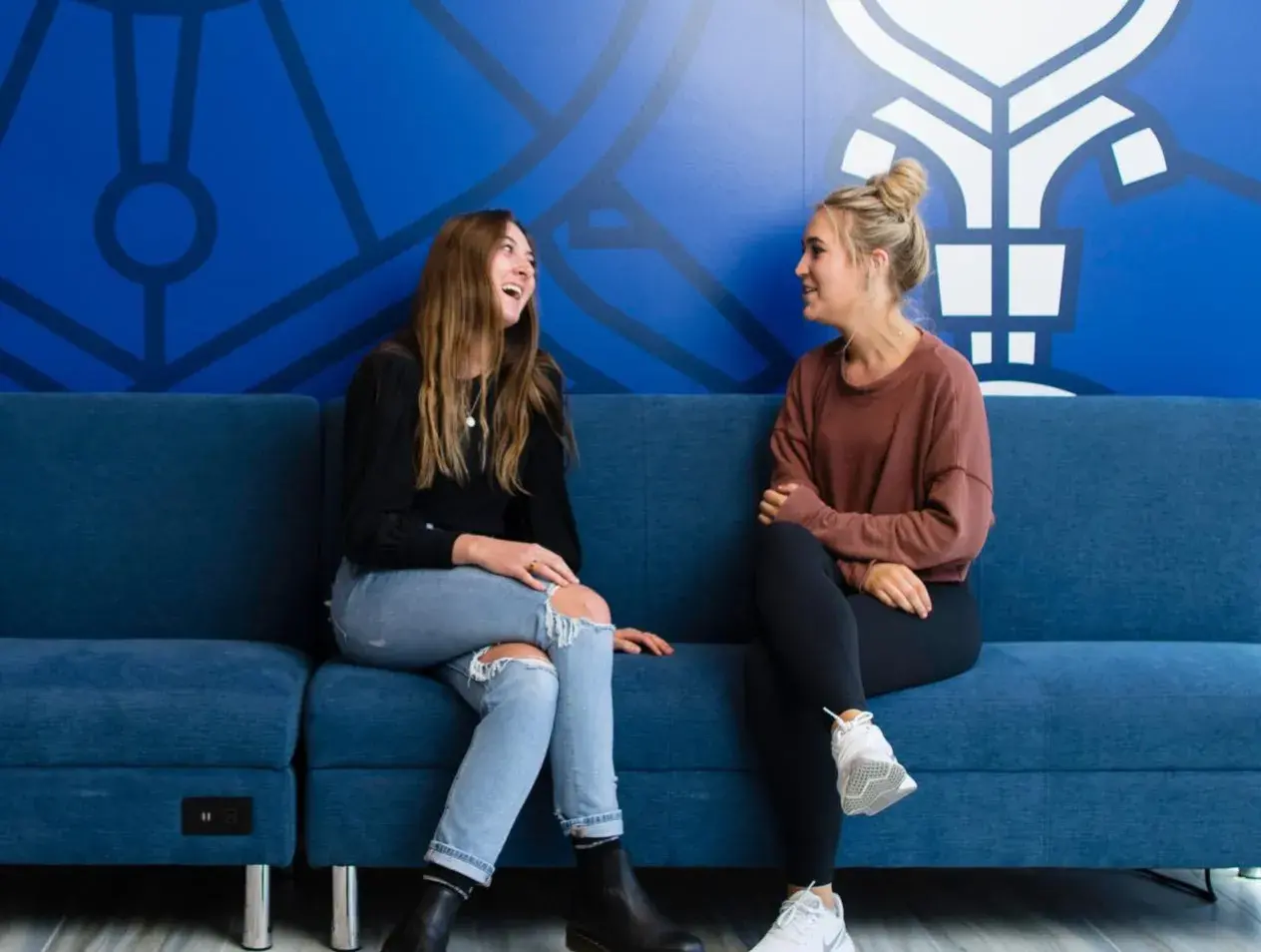 Two honors students engaging each other on a bench in an interior campus building.