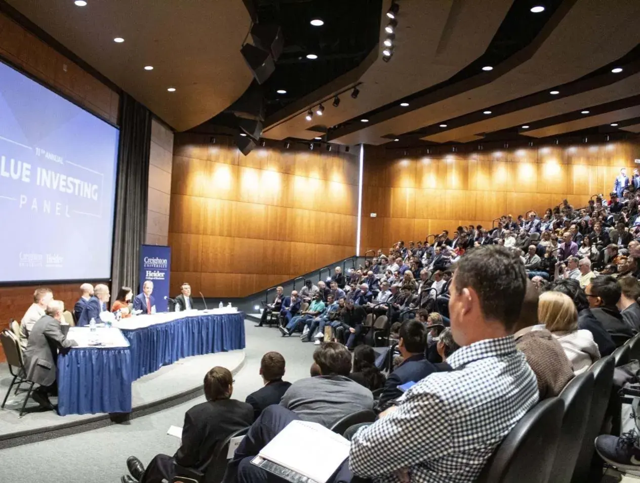 Value investing panel taking place in crowded auditorium.