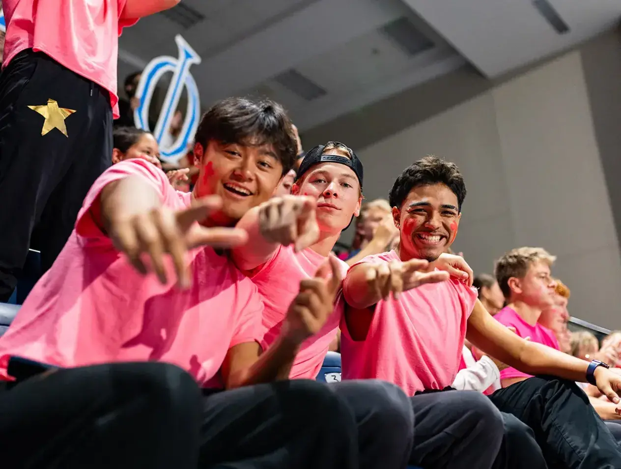 Fraternity brothers pointing at camera in pink shirts.