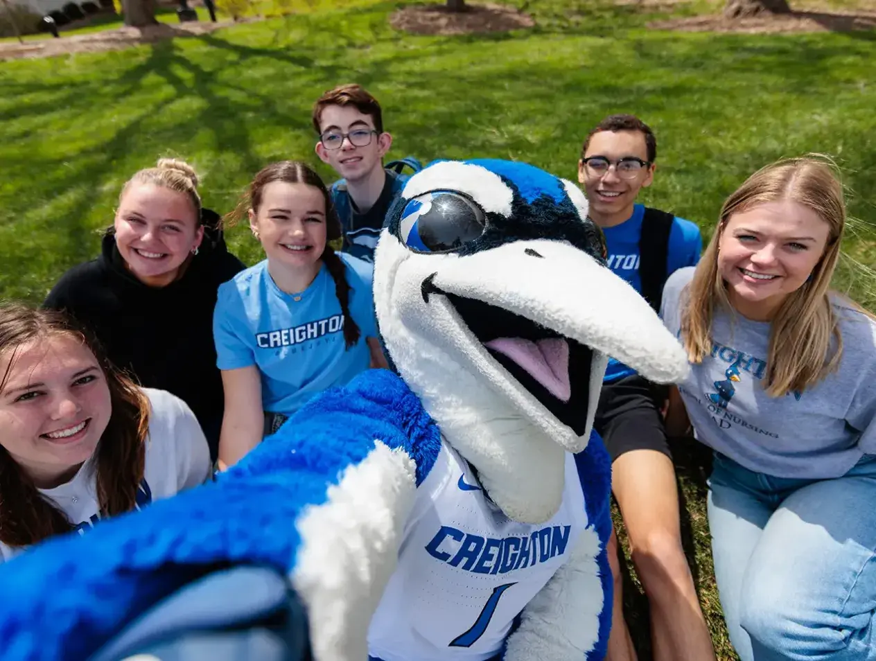 Billy Bluejay on campus lawn with students.