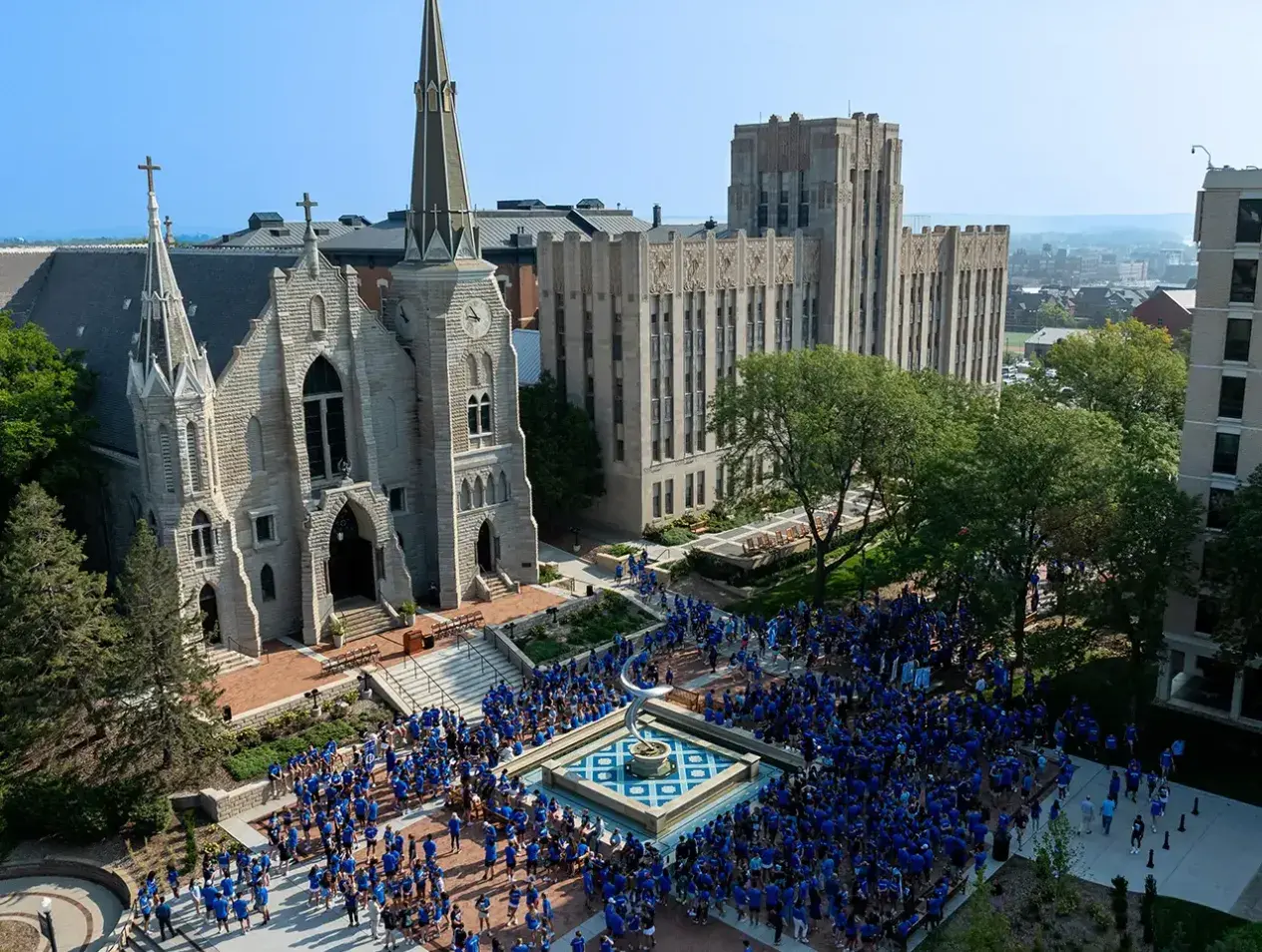 Wide shot from drone from above of St. John's church and mall area with students gathered in mass in Creighton blue t-shirts.