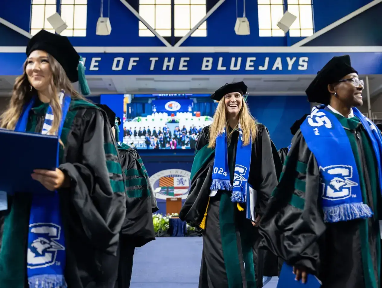 Three female graduates in regalia in front of stage
