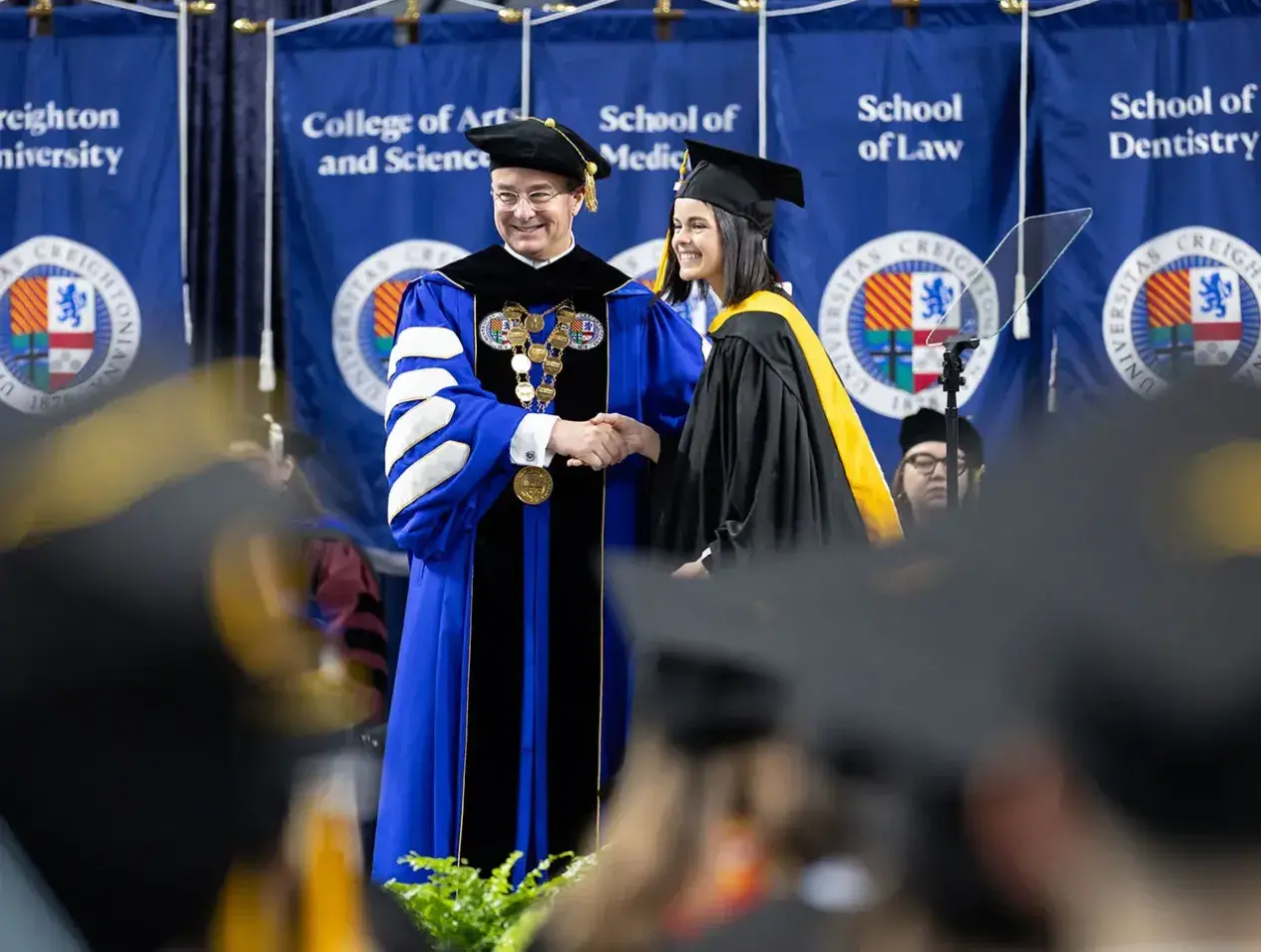 Female student shaking hands with Fr. Hendrickson on commencement stage