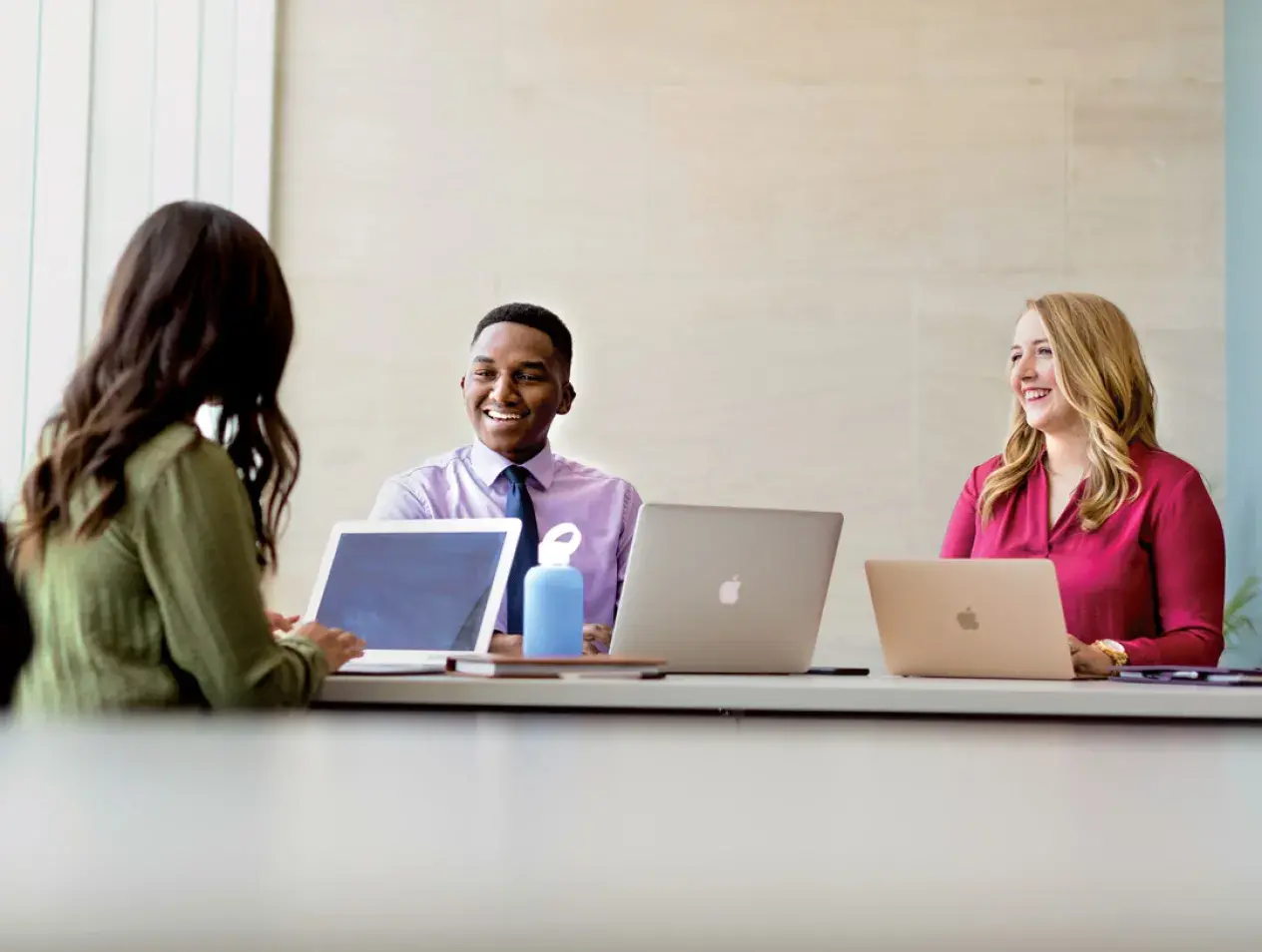 three students at a table talking with their laptops in front of them