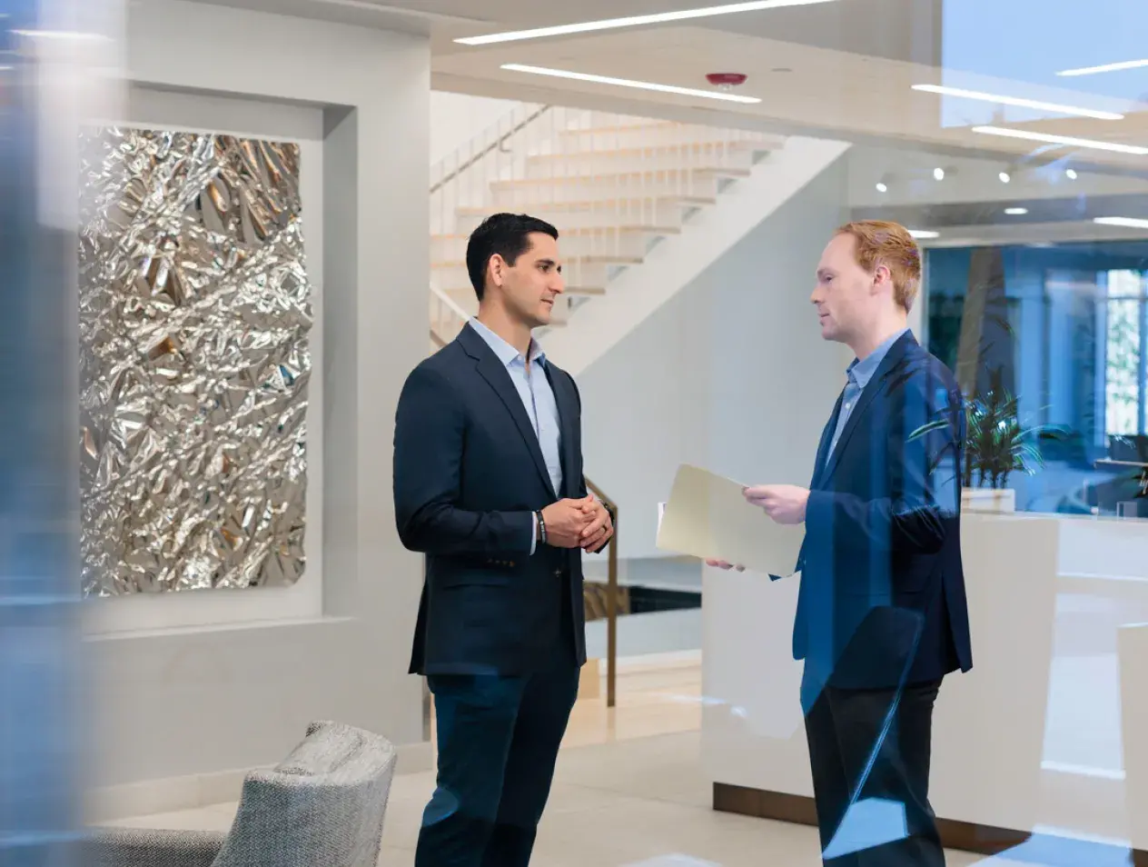 Two people standing, talking in an office lobby