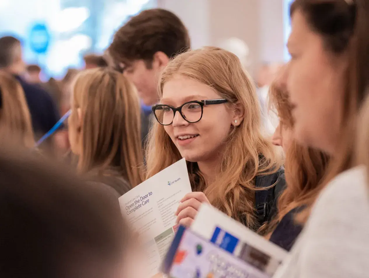 Student standing in a crowd listening and smiling