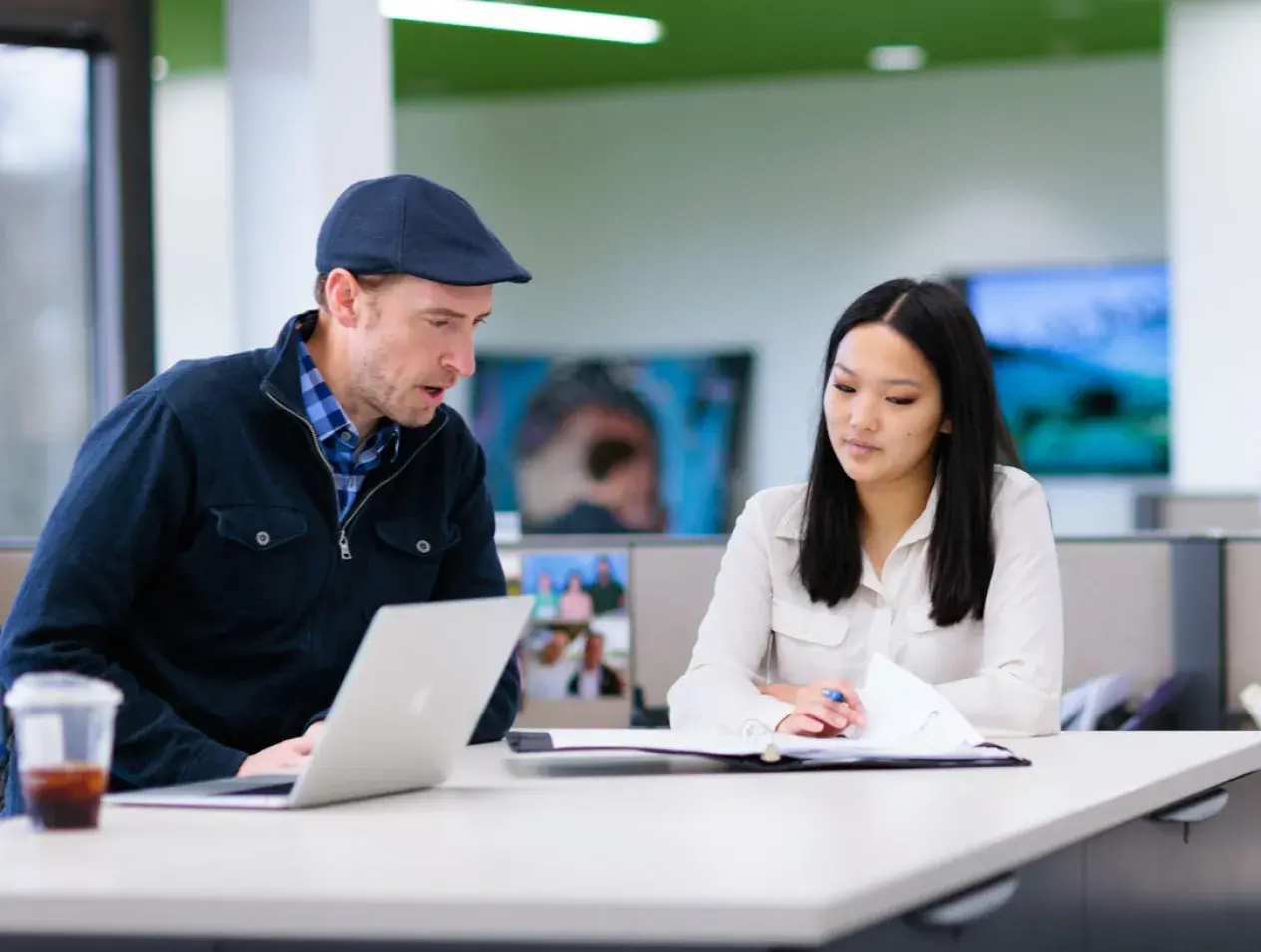 Student talking with man in a hat looking over a binder at a table