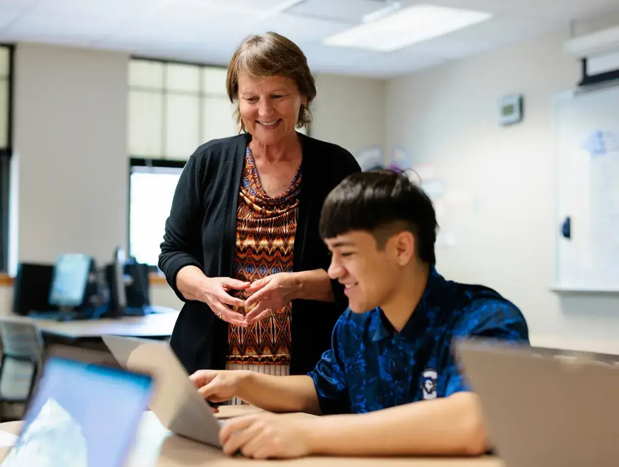 Staff member working with student on laptop.