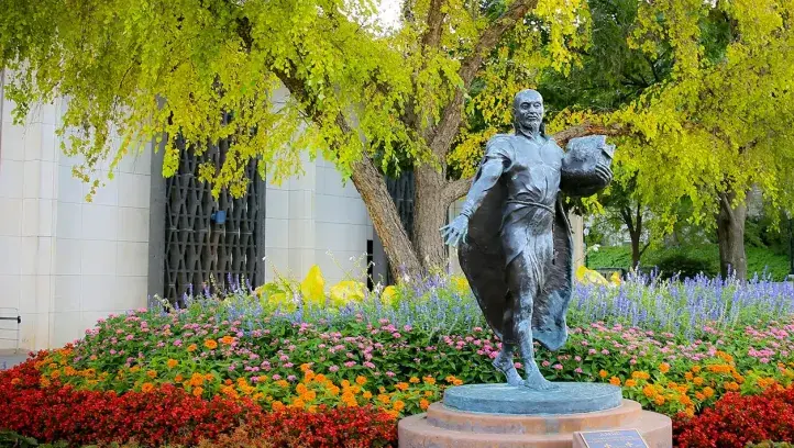 Jesuit statue amidst colorful flowers.