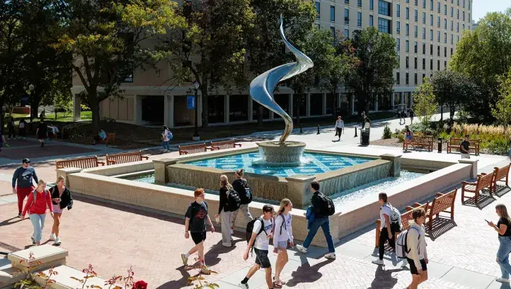 Students walking near flame fountain on mall.