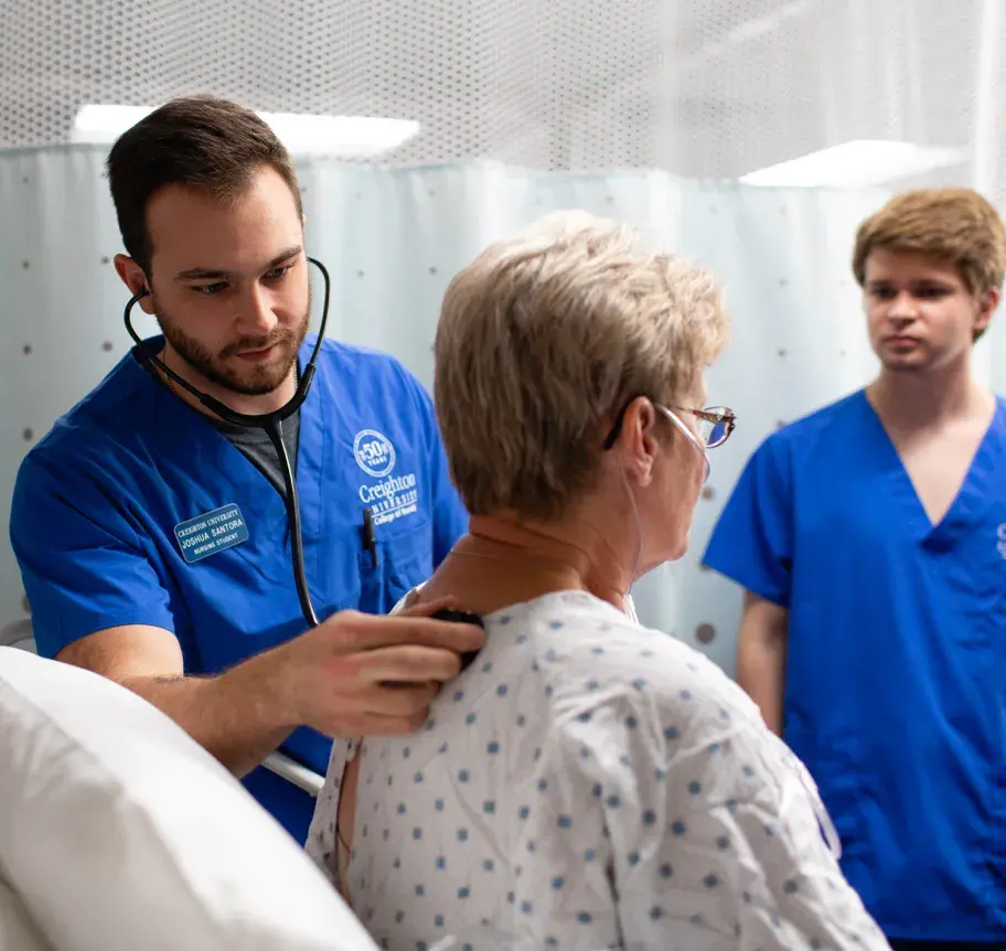 Male nursing student using stethescope on patient's back