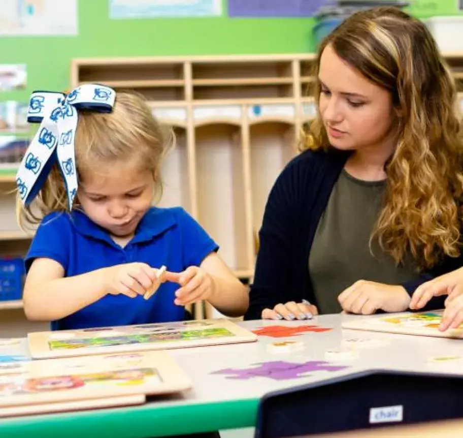 A teacher watches as a young student works on a puzzle