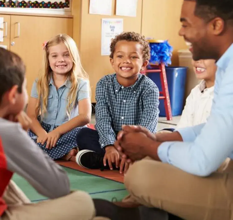 A teacher with a group of elementary students sitting in a circle on the floor