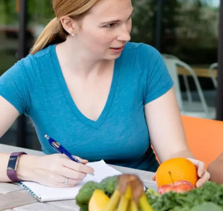 A woman holding an orange and writing in a notebook