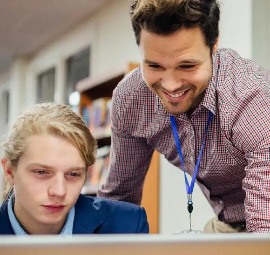 A teacher leaning over to assist a student on a computer
