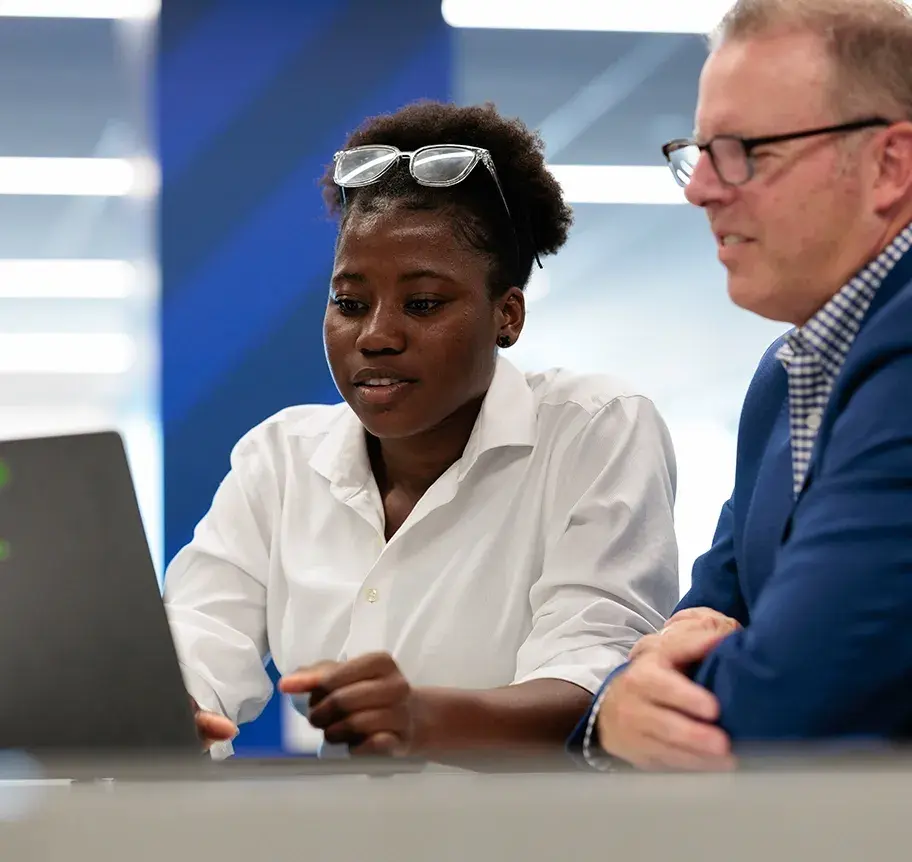 A Master of Accounting student reviews work on a laptop alongside a faculty member in a modern professional setting.