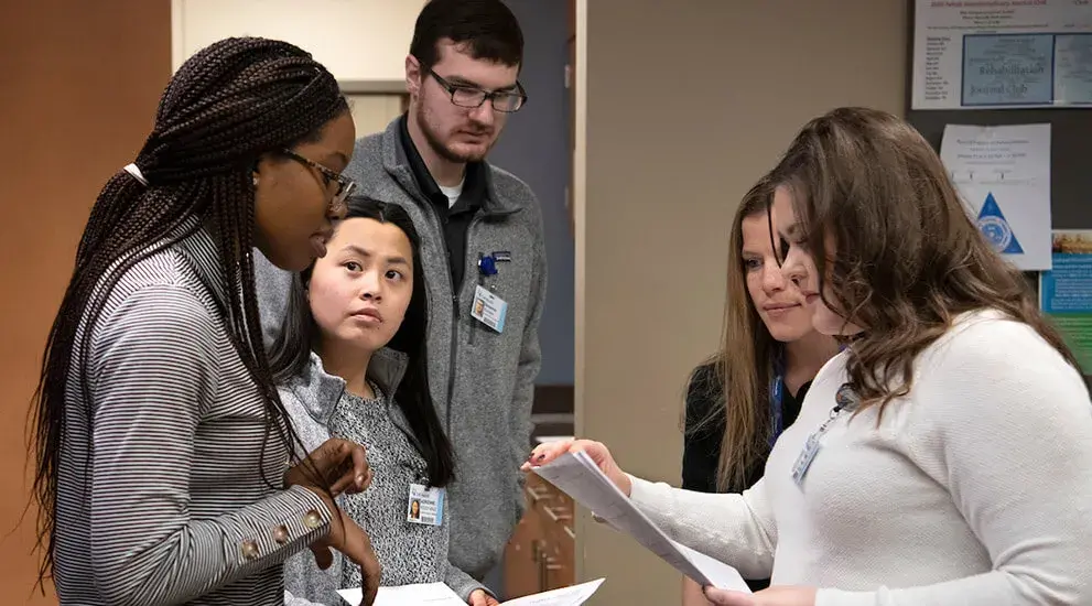 A group of physical therapy students standing and discussing paperwork