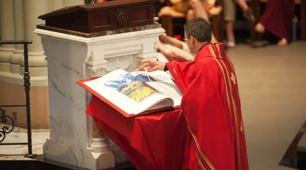 A priest moves the page marker of the St. John's Bible during Mass