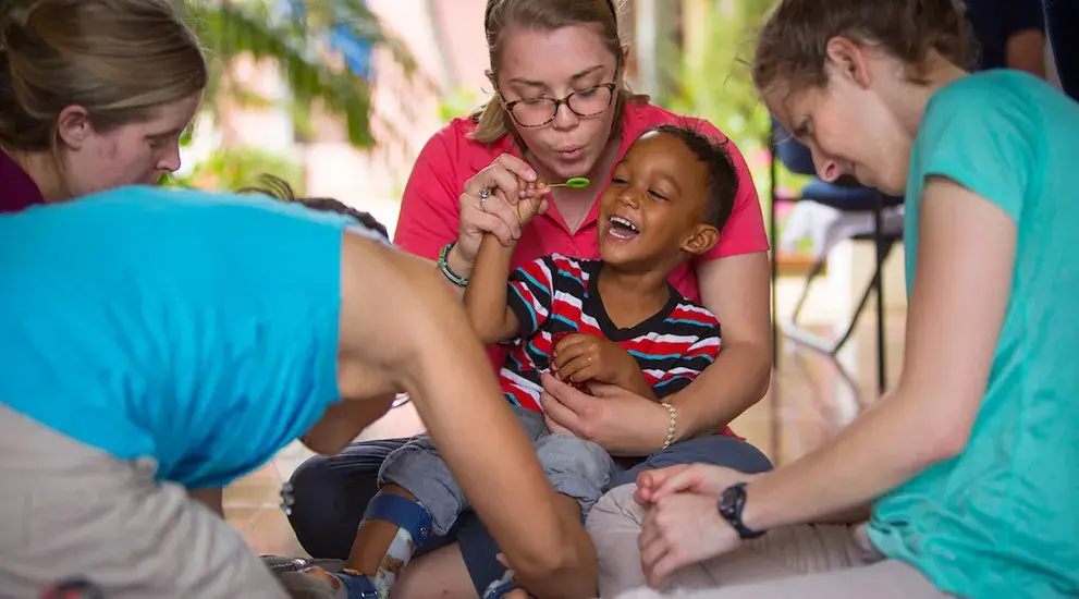 Students in the Encuentro Dominicano program helping a young boy with leg braces